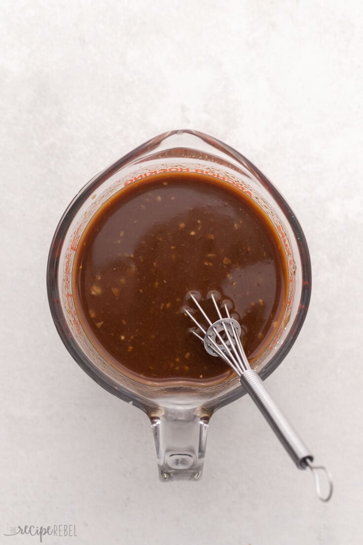 glass measuring cup filled with sauce and steel whisk.