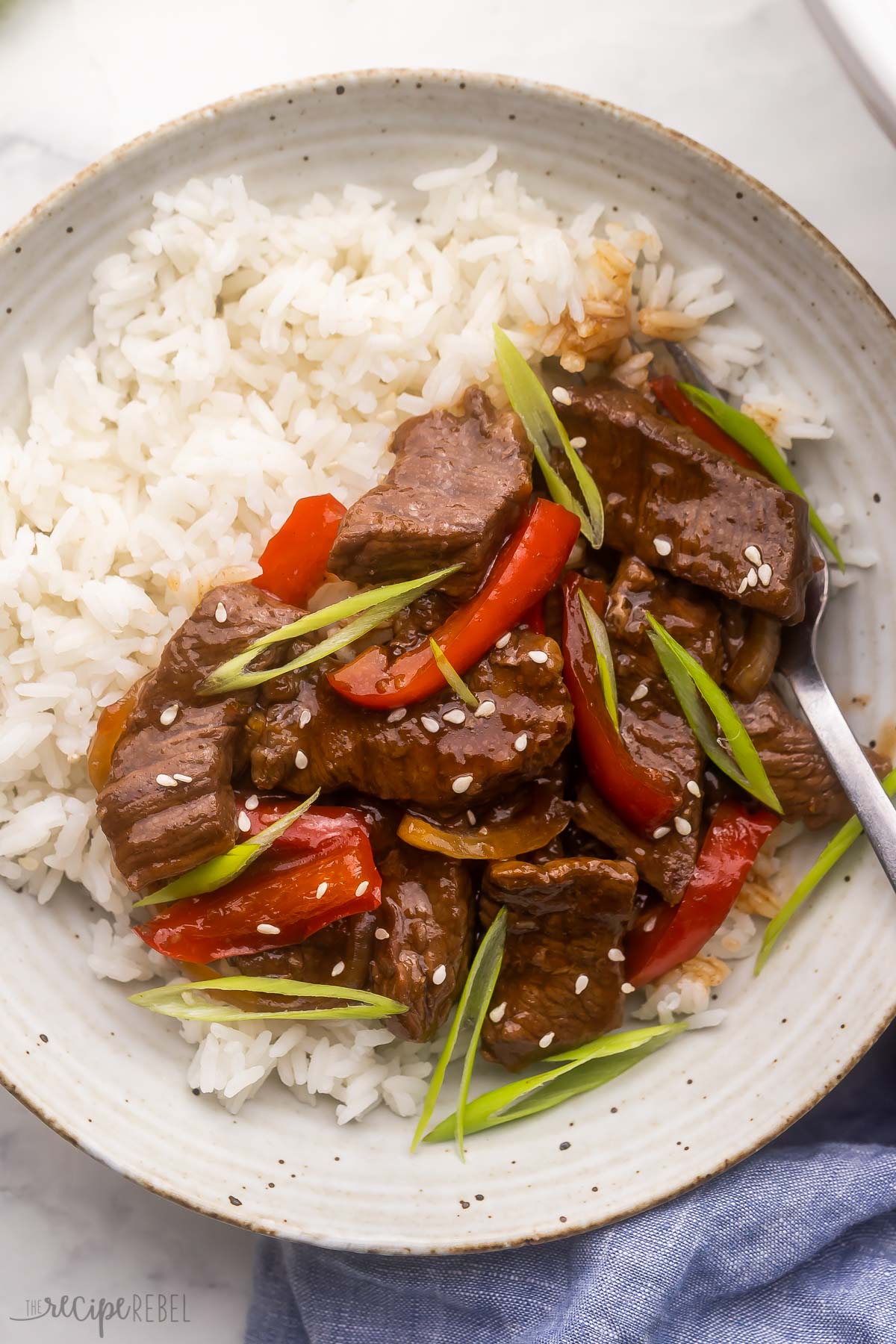 mongolian beef on rice in a white bowl with a fork.