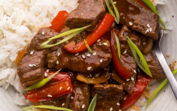 close up of mongolian beef on rice topped with sesame seeds.