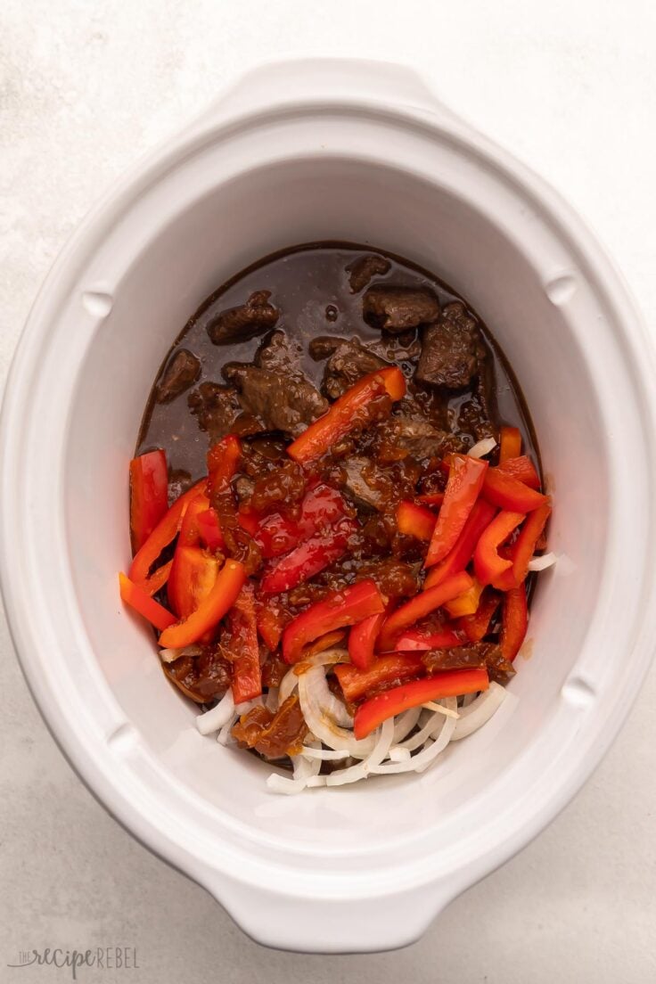 white slow cooker filled with beef, sauce, and vegetables.