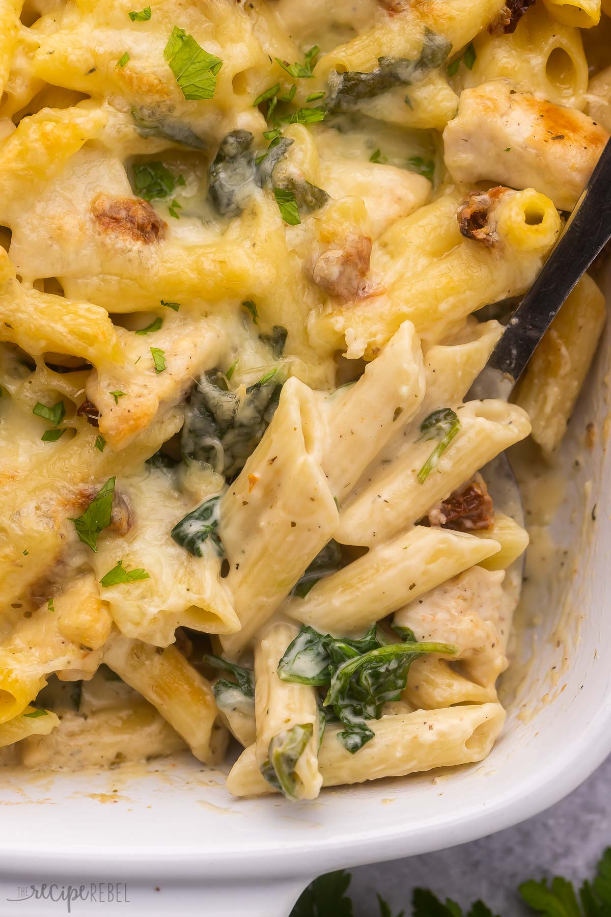close up of a scoop of tuscan chicken pasta bake in white dish.
