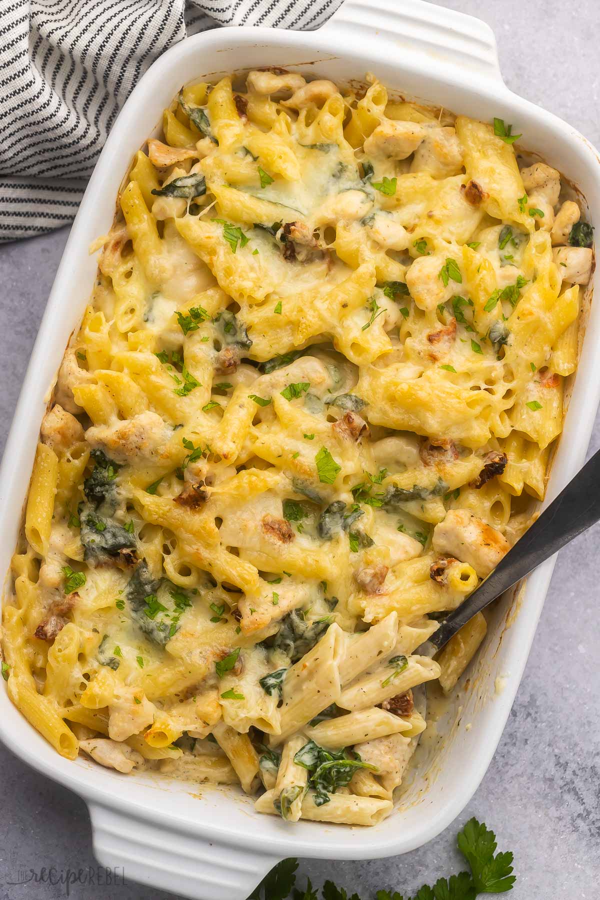 large white baking dish filled with tuscan chicken pasta bake and steel ladle.