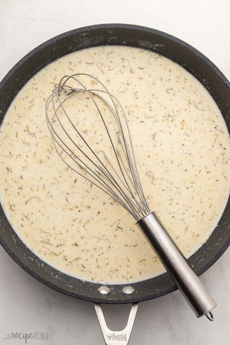 black frying pan filled with cream sauce ingredients and steel whisk.
