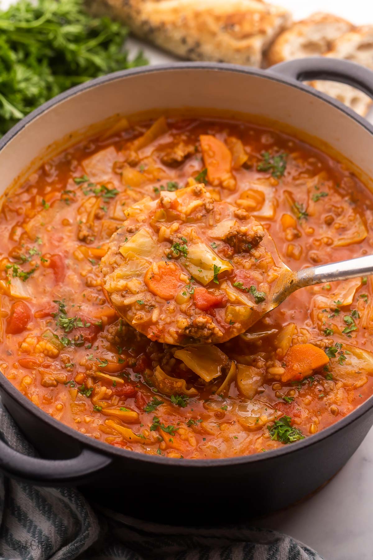 Cabbage Roll Soup is a one pot soup recipe that's made hearty with ground beef and of course plenty of tender cabbage! A bold tomato broth holds it all together and makes every spoonful more savory than the last. #soup #dinner #recipe | soup recipe | cabbage soup | ground beef soup | healthy soup | cabbage recipe | easy dinner ideas pot of cabbage roll soup with metal ladle scooping some soup.