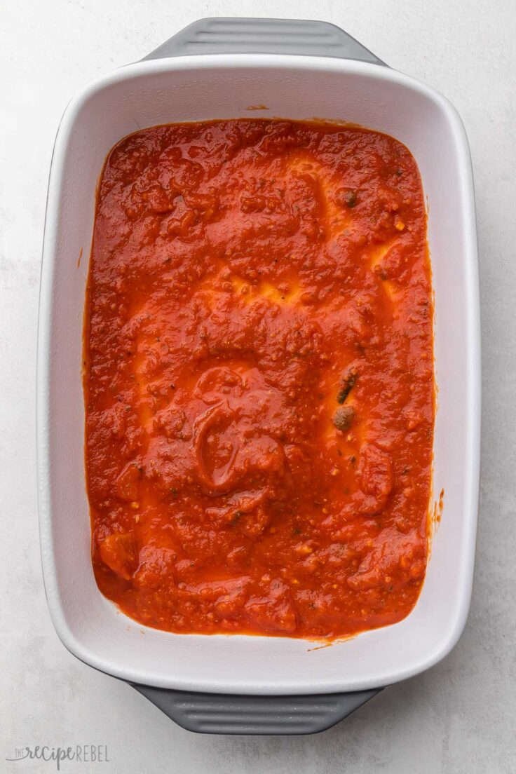 white baking dish with tomato sauce spread across bottom.