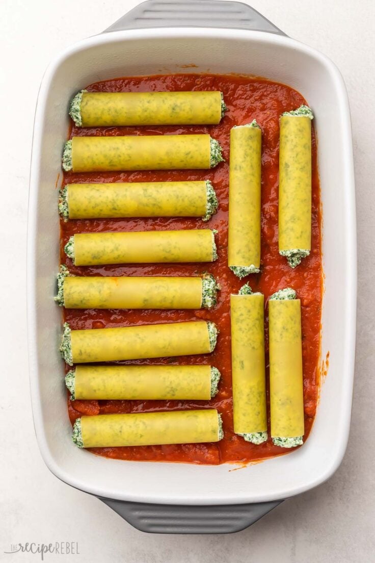 large white baking dish with filled cannelloni lying in bottom.