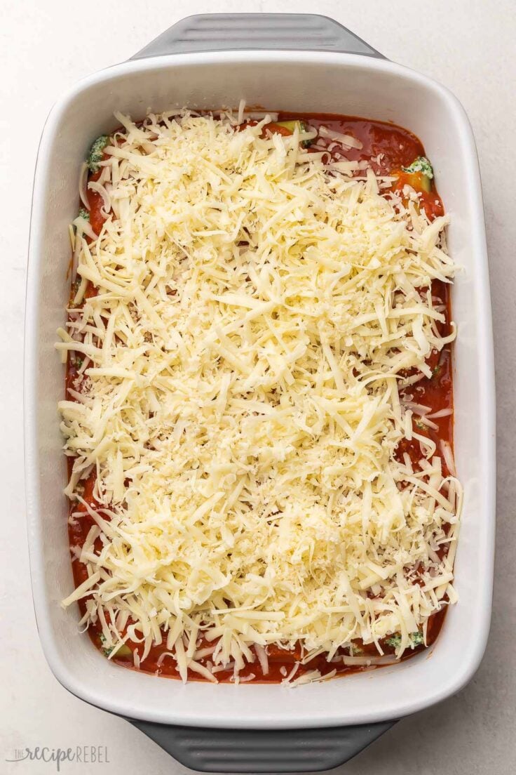 shredded cheese added to cannelloni in white baking dish.