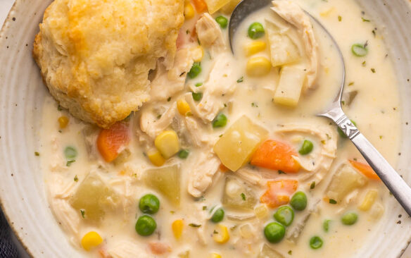 close up of a bowl of chicken pot pie soup with a biscuit on the edge.