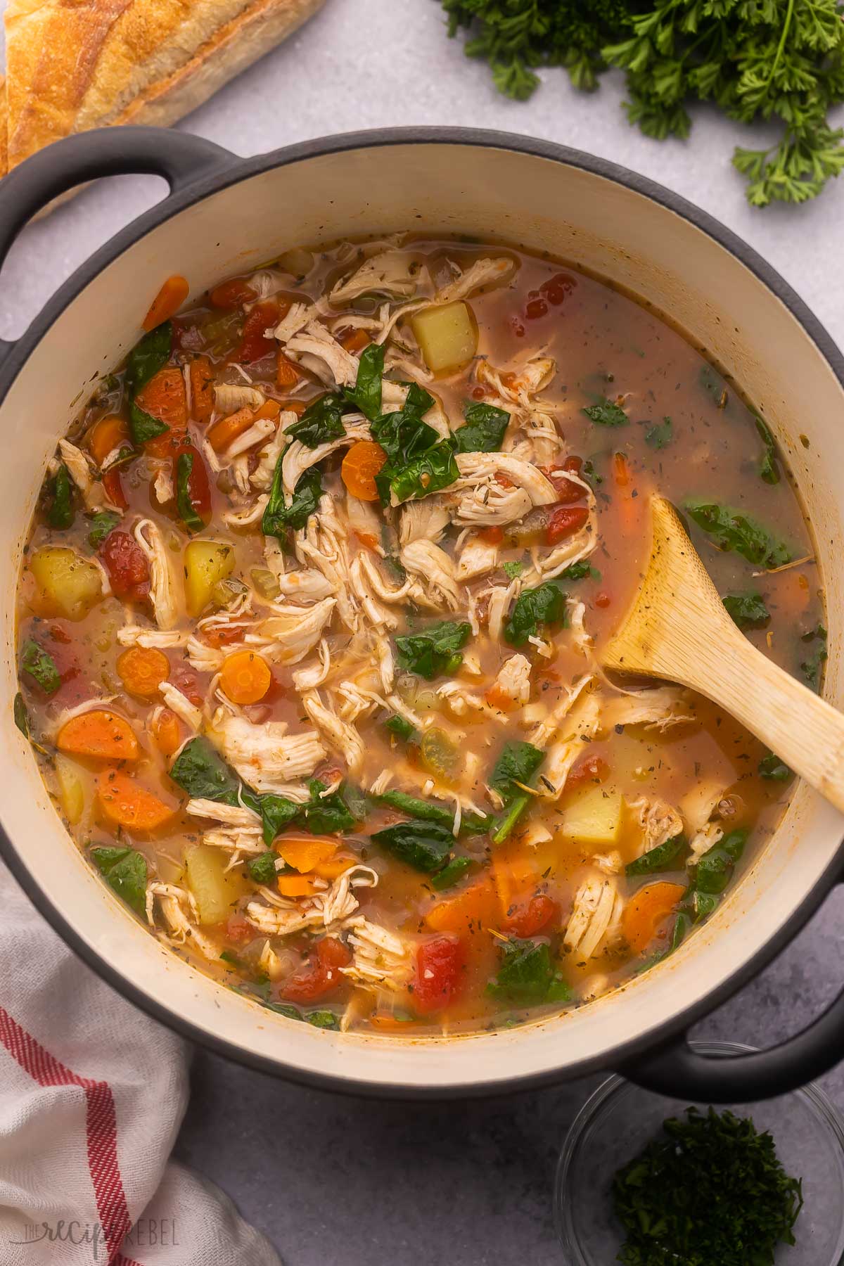 large pot filled with chicken vegetable soup and wooden ladle.