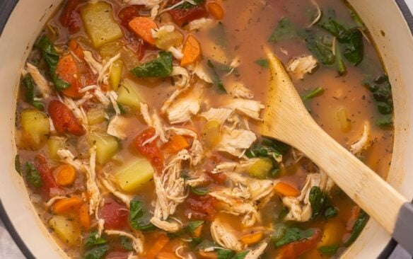 close up of chicken vegetable soup in large black pot.