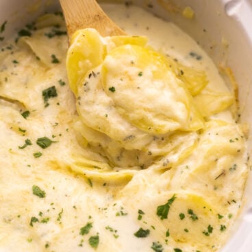 scoop of crockpot scalloped potatoes coming out of white crockpot.