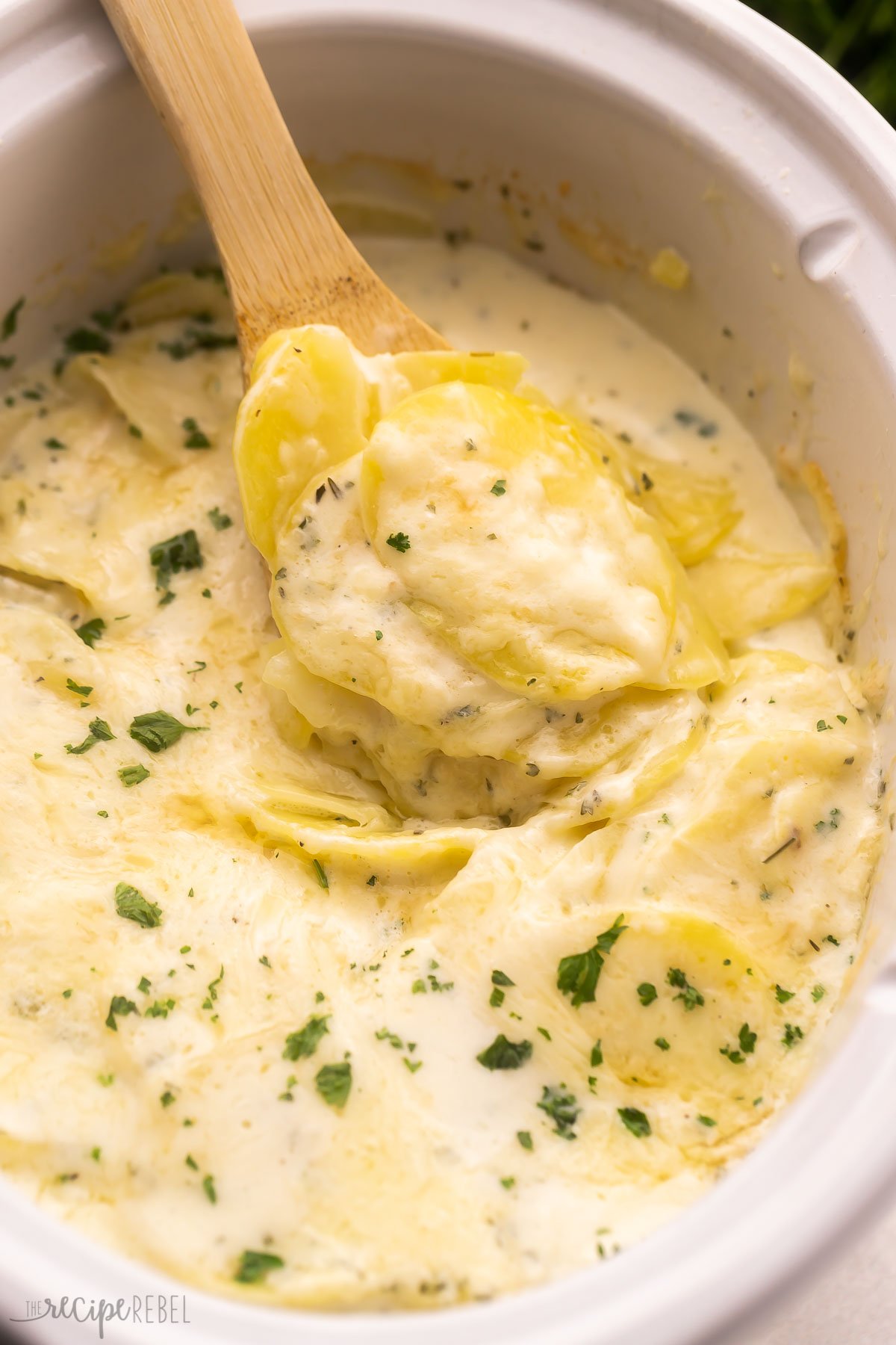 scoop of crockpot scalloped potatoes coming out of white crockpot.