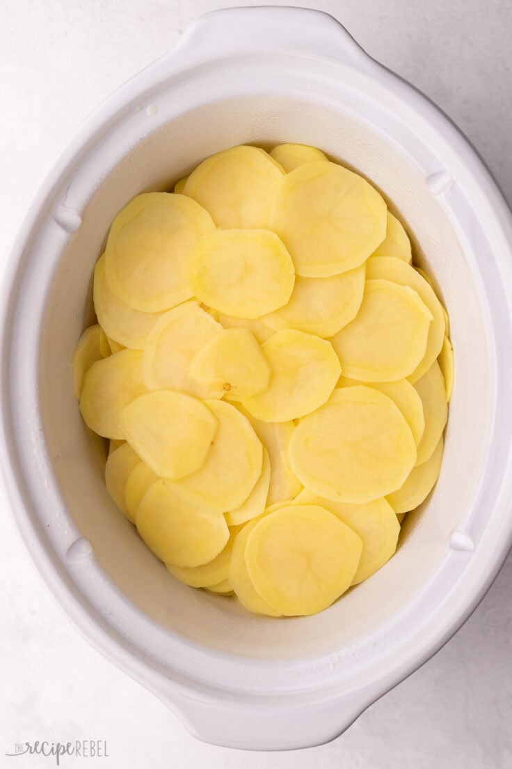 white crockpot full of sliced potatoes.