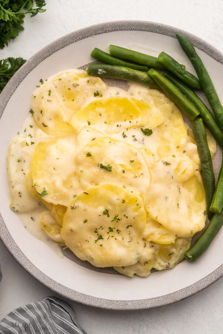 plate full of scalloped potatoes and green beans on grey surface.