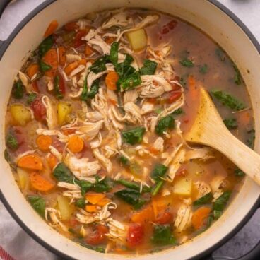 large pot filled with chicken vegetable soup and wooden ladle.