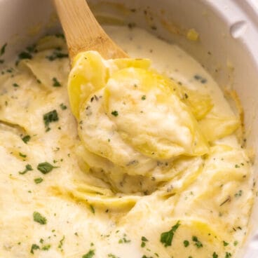 scoop of crockpot scalloped potatoes coming out of white crockpot.