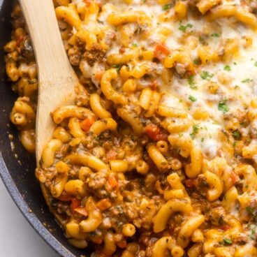 black pan filled with homemade hamburger helper and a wooden ladle in it.