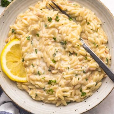 speckled bowl of lemon orzo with a slice of lemon on the side.