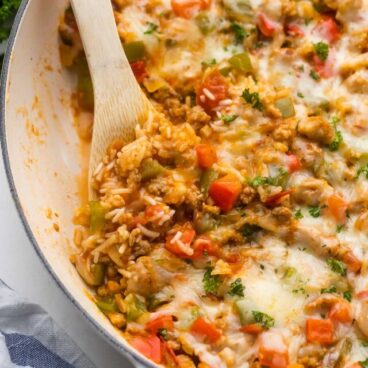 wooden ladle scooping stuffed pepper casserole out of white dish.