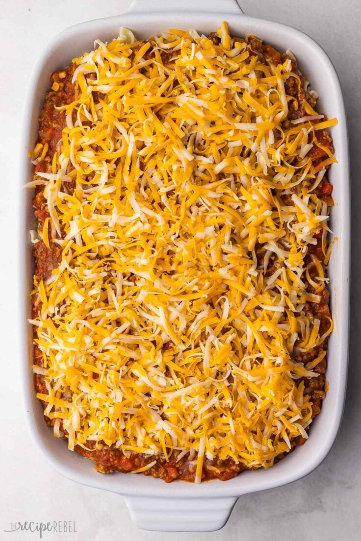 ground beef casserole in white dish with shredded cheese added to top.