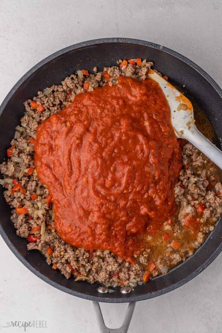 cooked ground beef in black pan with tomato sauce added on top.