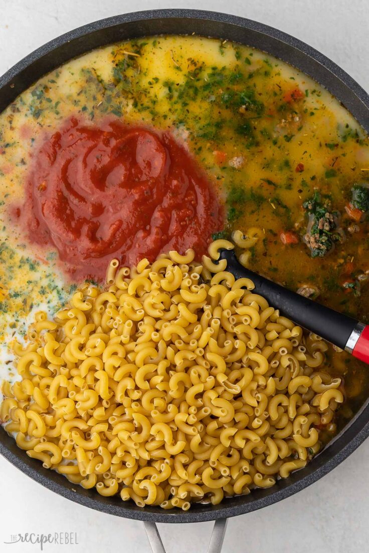 black pan filled with ingredients topped with pasta and tomato sauce.
