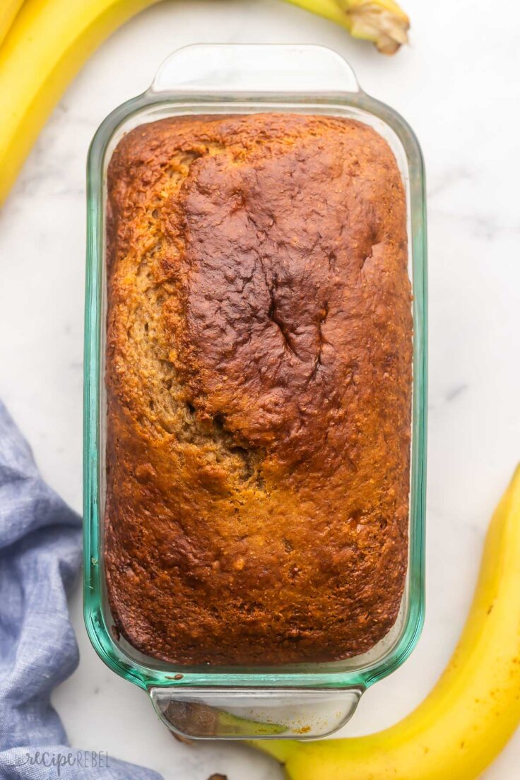 baked loaf of banana bread on grey surface with bananas beside.