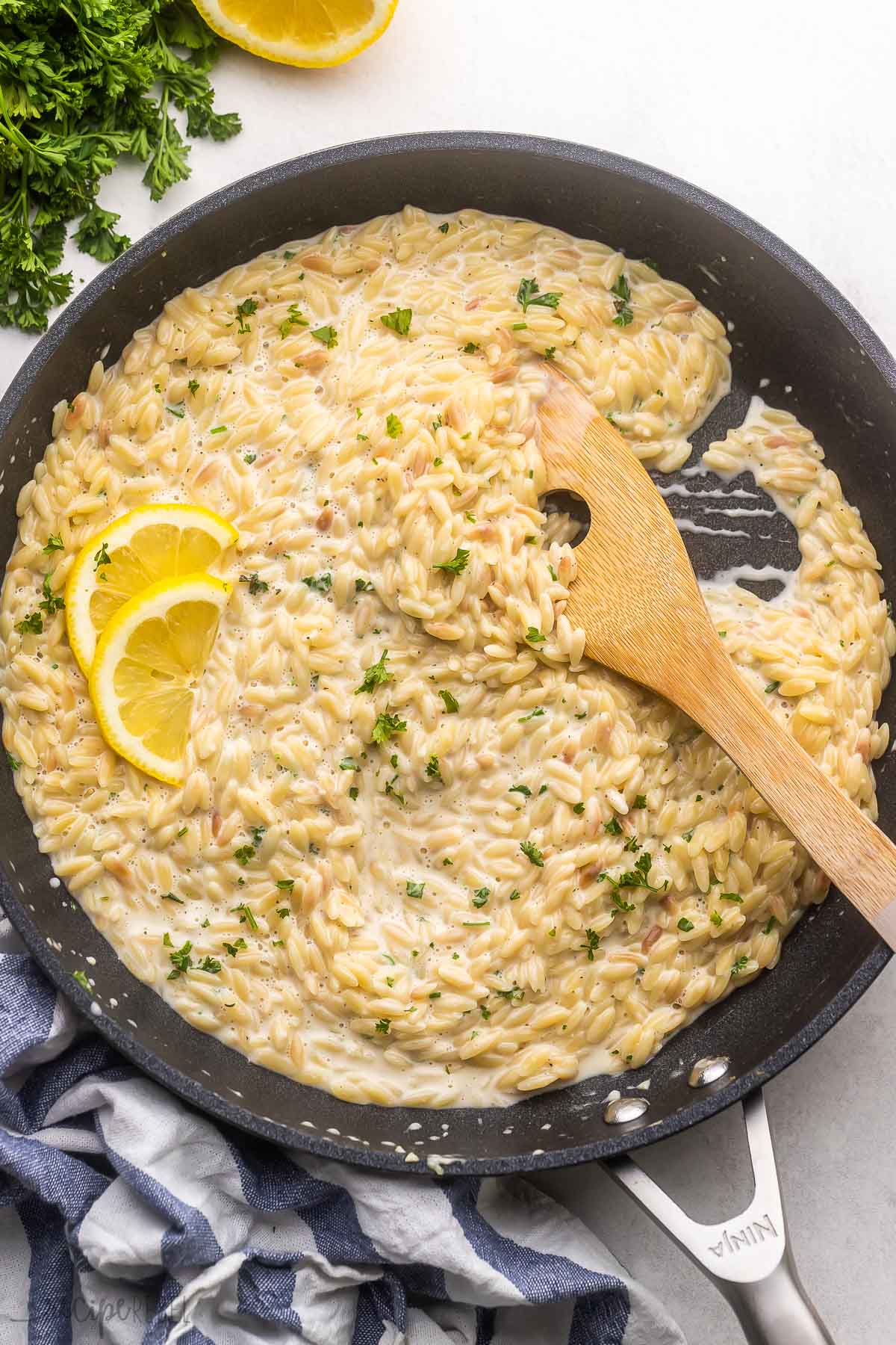 large black pan of lemon orzo pasta with lemon slices beside.