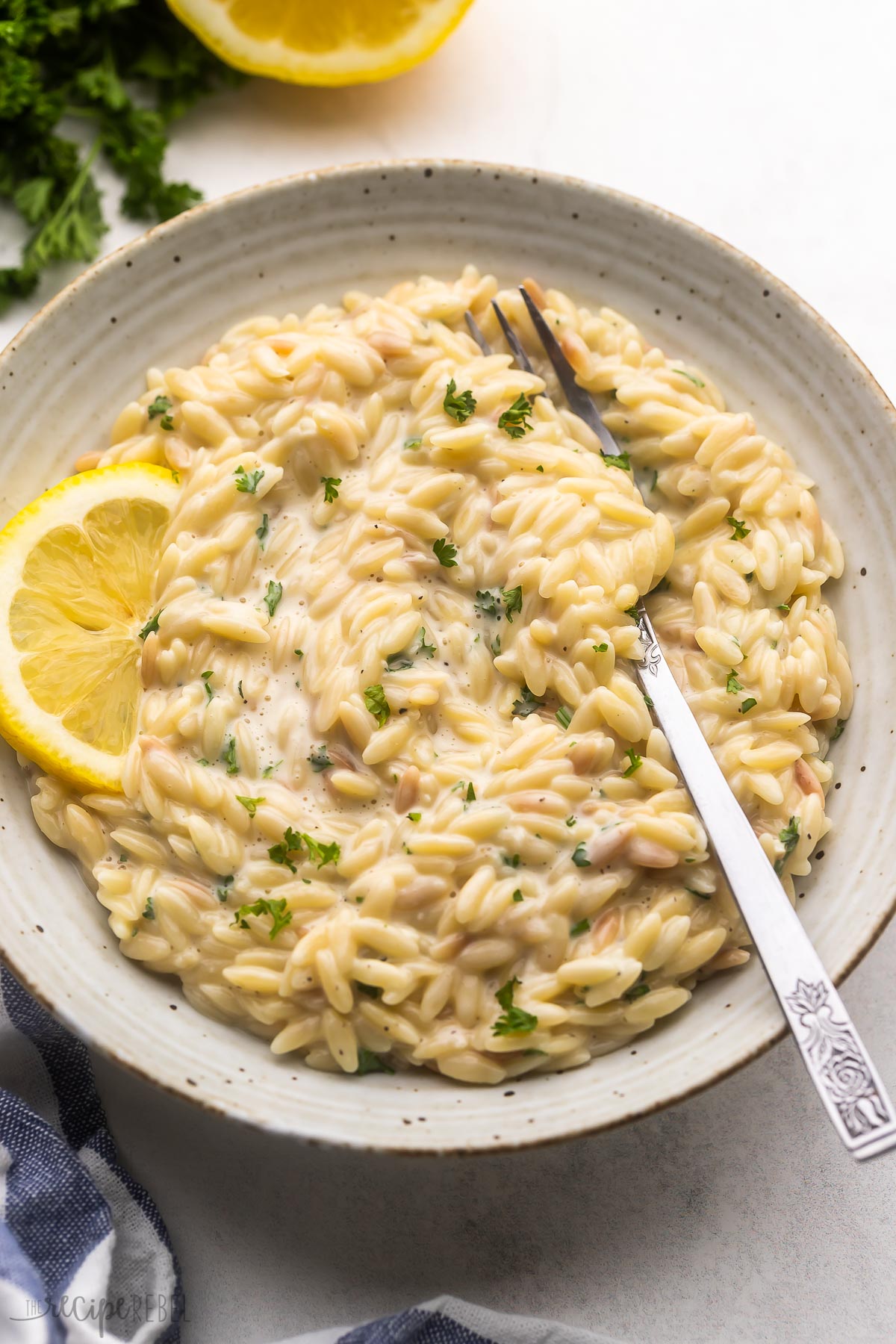 a fork in a bowl of lemon orzo pasta with a lemon slice beside.