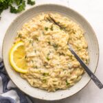 close up of creamy lemon orzo in a bowl with fork and lemon slice.
