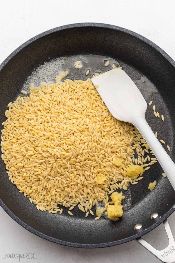 orzo and garlic in black pan with spatula.