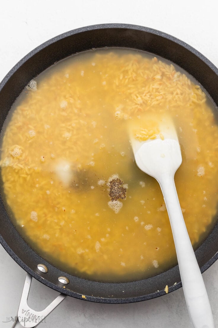 broth added to ingredients in black pan with spatula alongside.