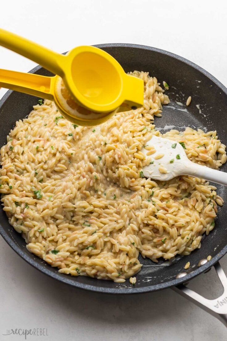 a lemon being squeezed above black pan with orzo in it.