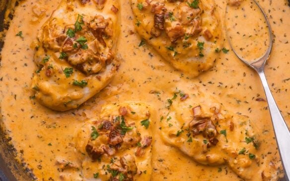 black pan with a spoon and four chicken breasts in marry me sauce.