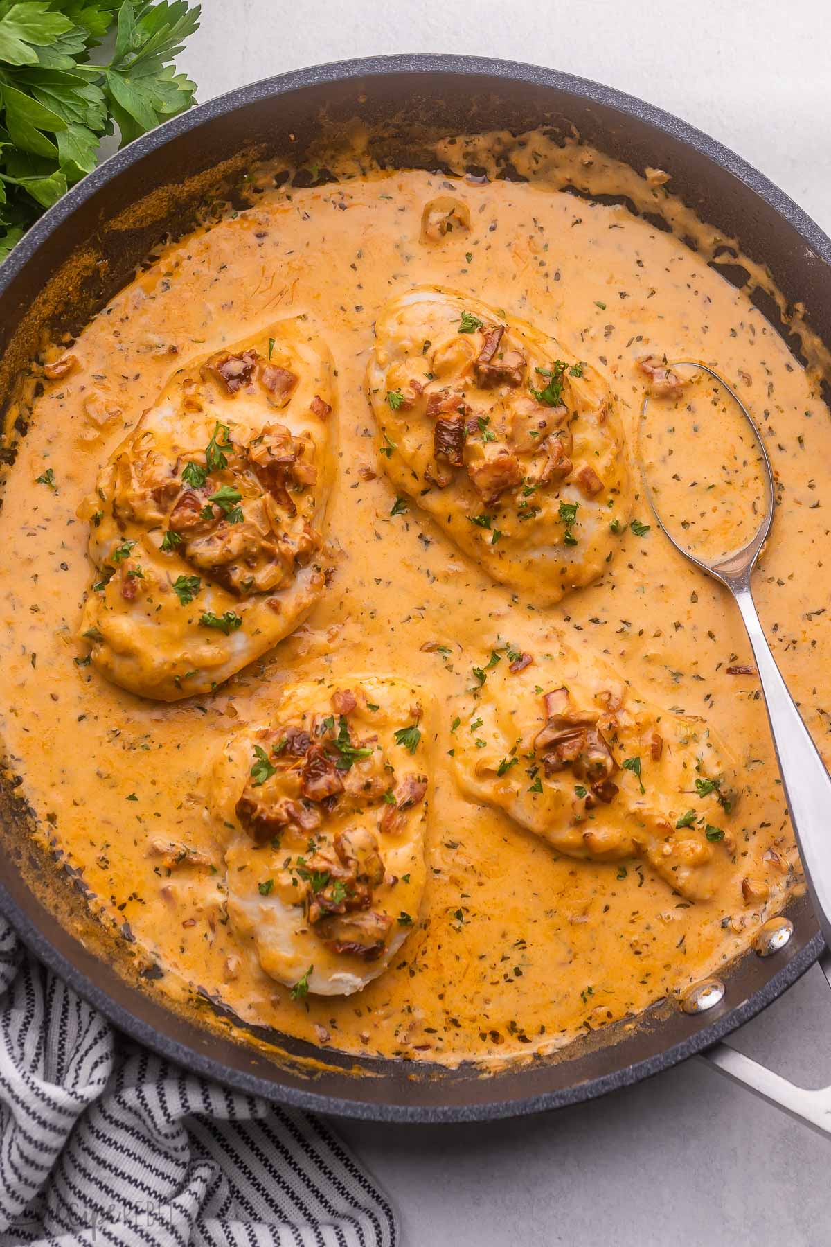 Marry Me Chicken features golden chicken breasts simmered in a medley of bold ingredients like bacon, garlic, sun-dried tomatoes and more! This one pan chicken recipe is served smothered in a creamy sauce that's so good, you may just hear wedding bells. #chicken #dinner | dinner ideas | dinner recipes | easy recipe | chicken dinner | chicken breast recipe | skillet chicken | creamy chicken overhead view of marry me chicken in black pan with parsley beside.