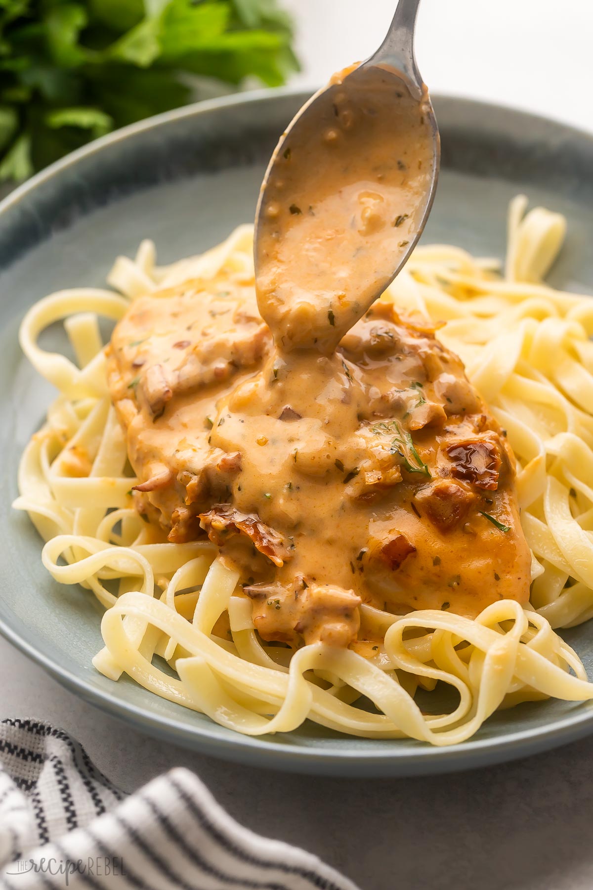 a blue dish with pasta and sauce being spooned on.