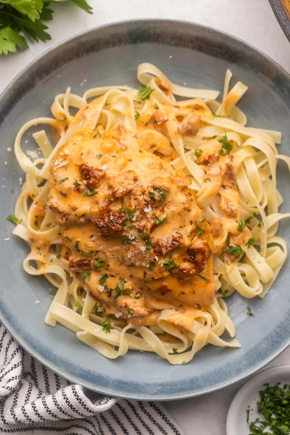 a blue plate filled with pasta and topped with marry me chicken.