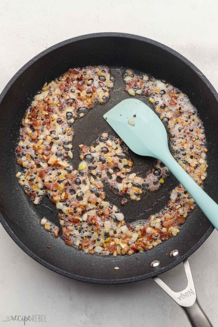 black pan filled with cooking bacon and onions.