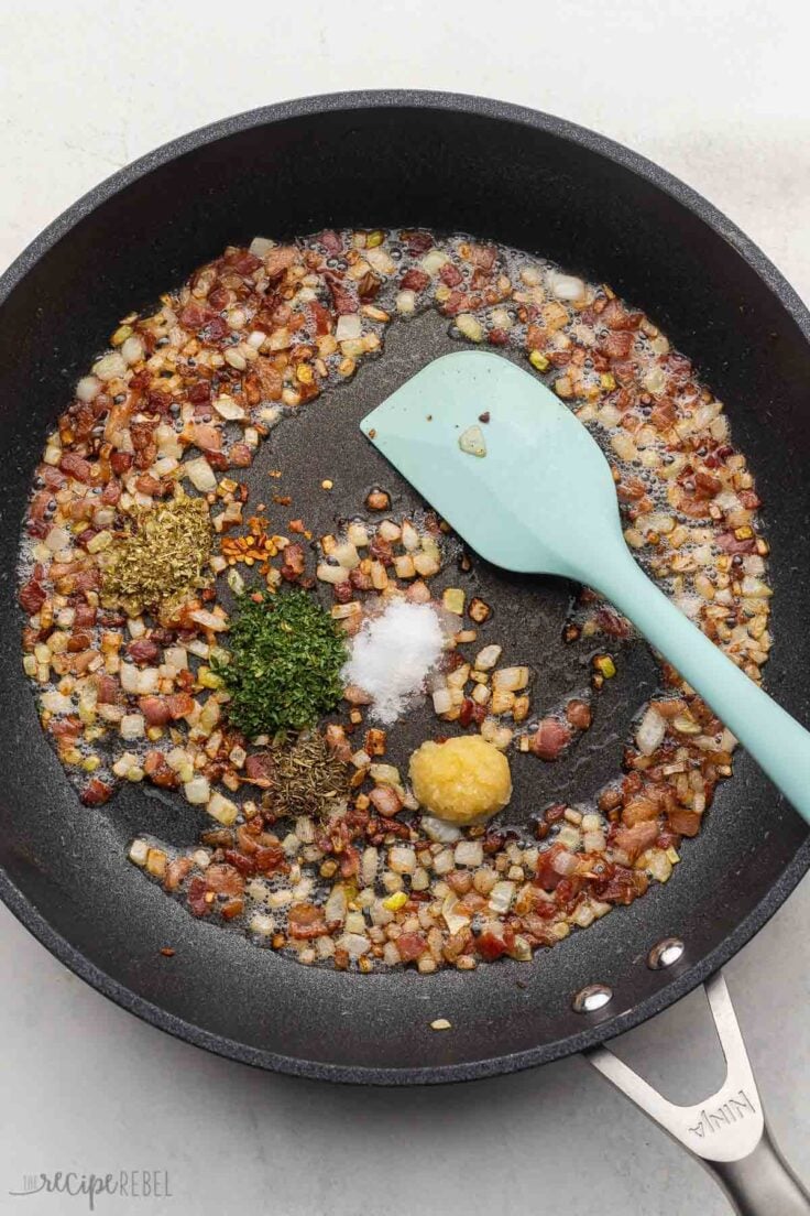 cooked ingredients and blue spatula in black pan with spices added.