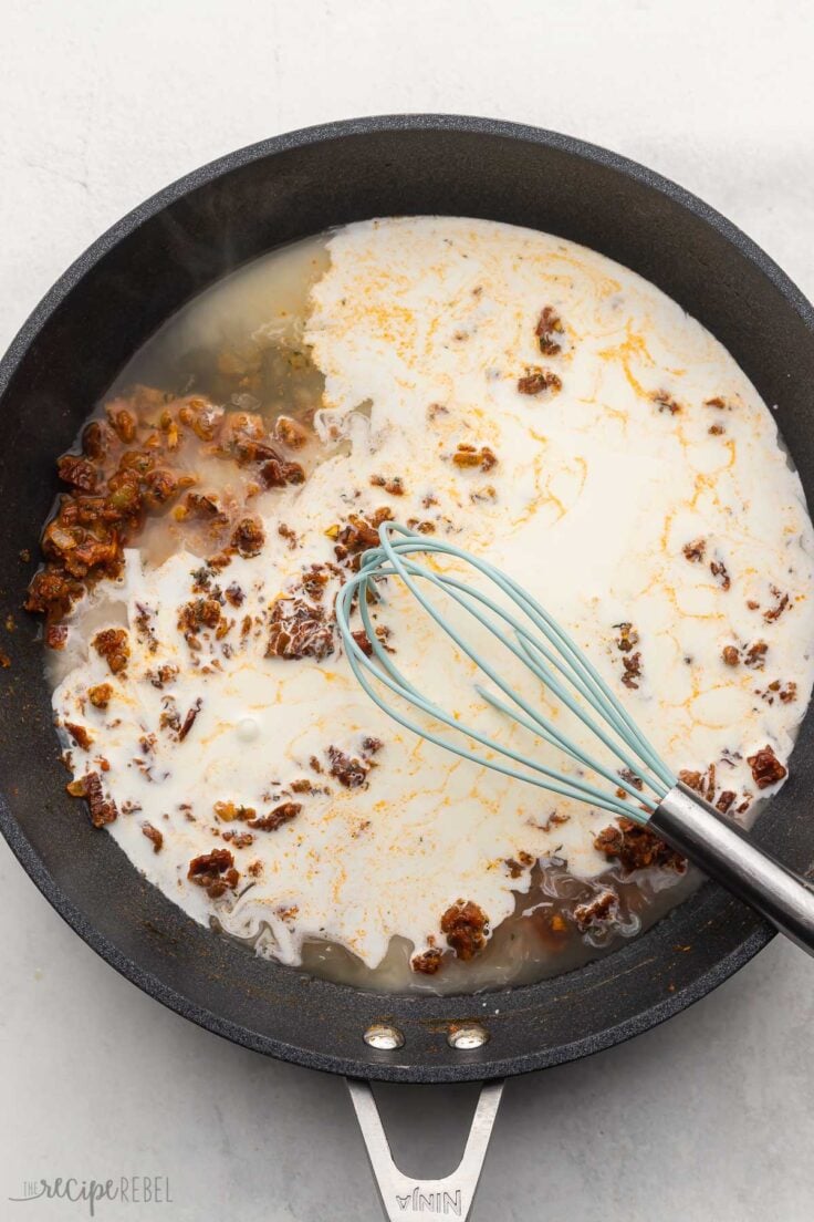 cream and broth added to cooked ingredients in black pan with whisk in it.