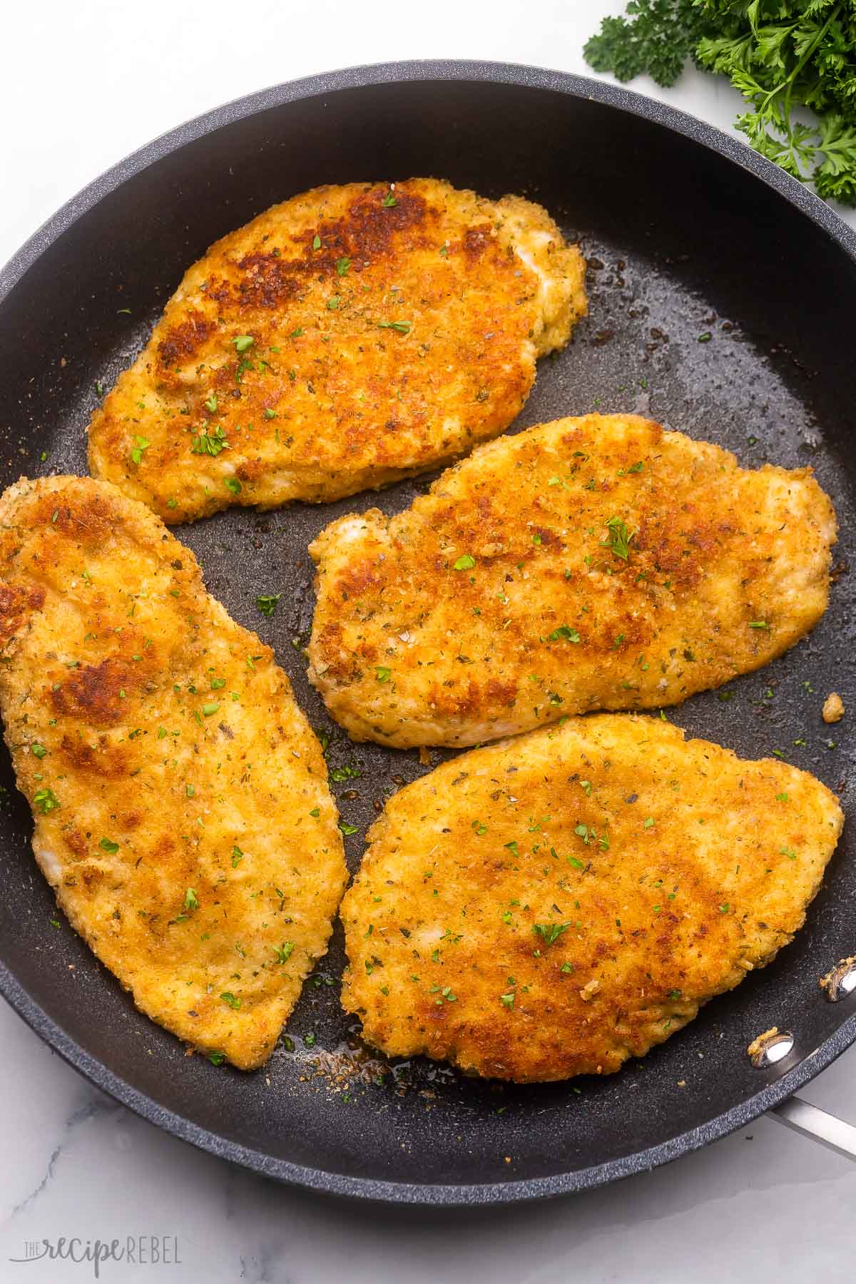 overhead view of four golden parmesan crusted chicken breasts in black pan.