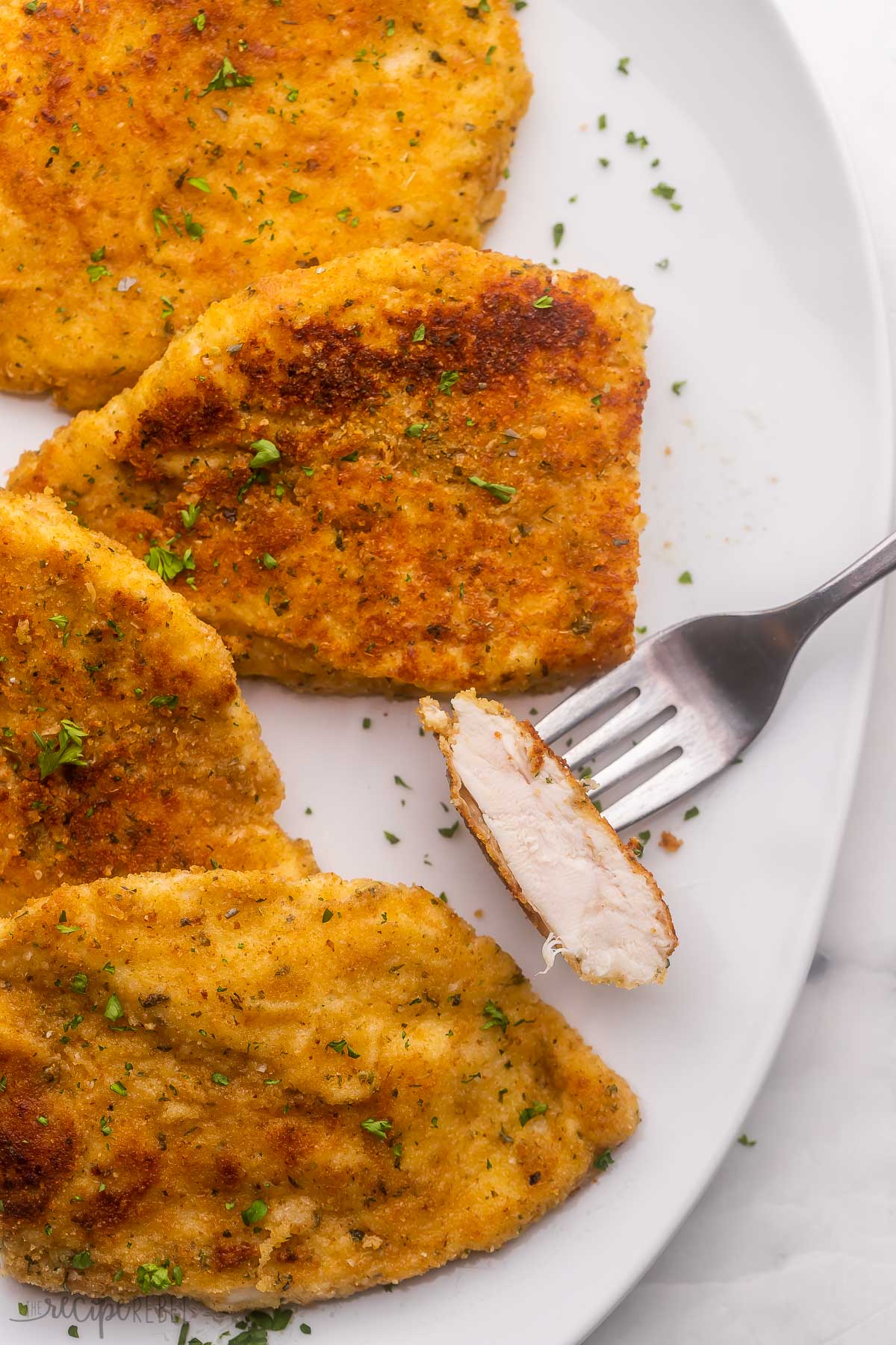 cooked chicken on a white plate with a piece on a fork.