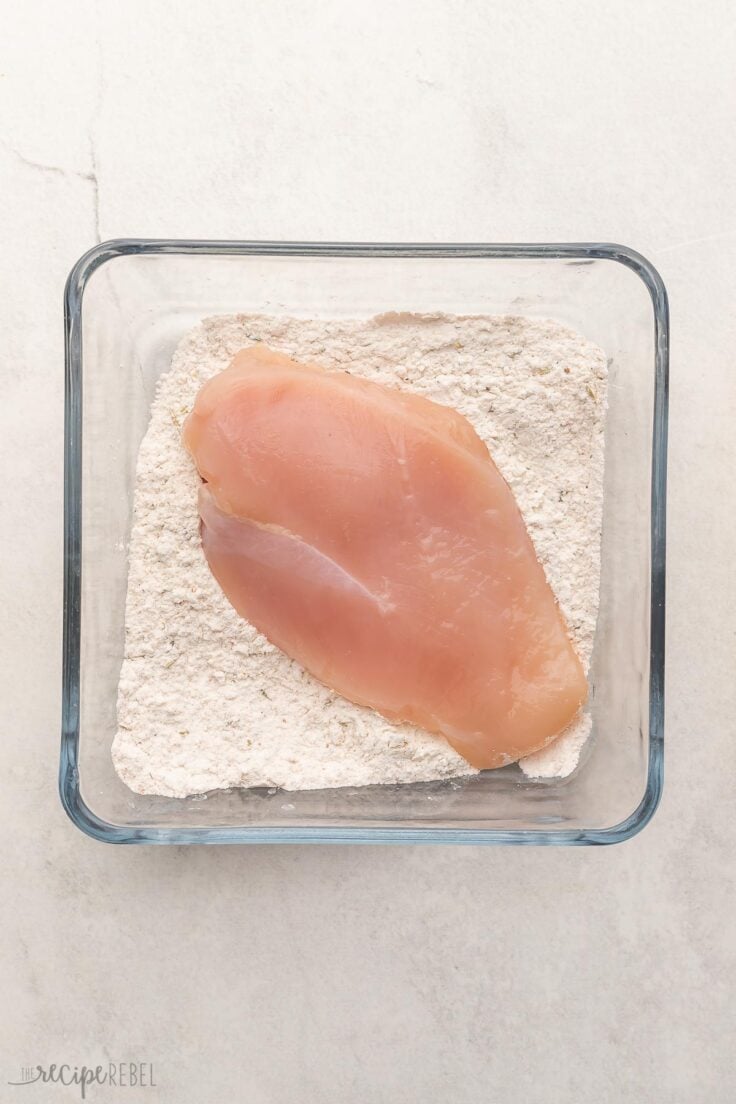 one chicken breast lying in a glass dish with flour.