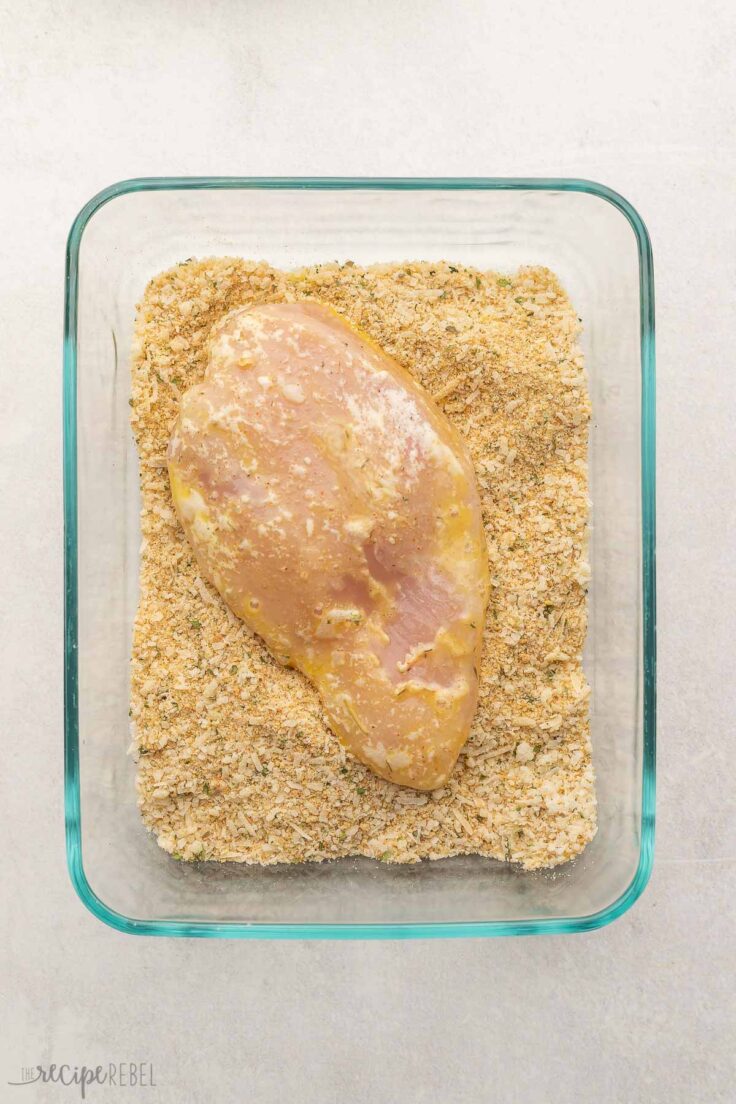 one chicken breast with egg coating lying in glass dish with seasonings.