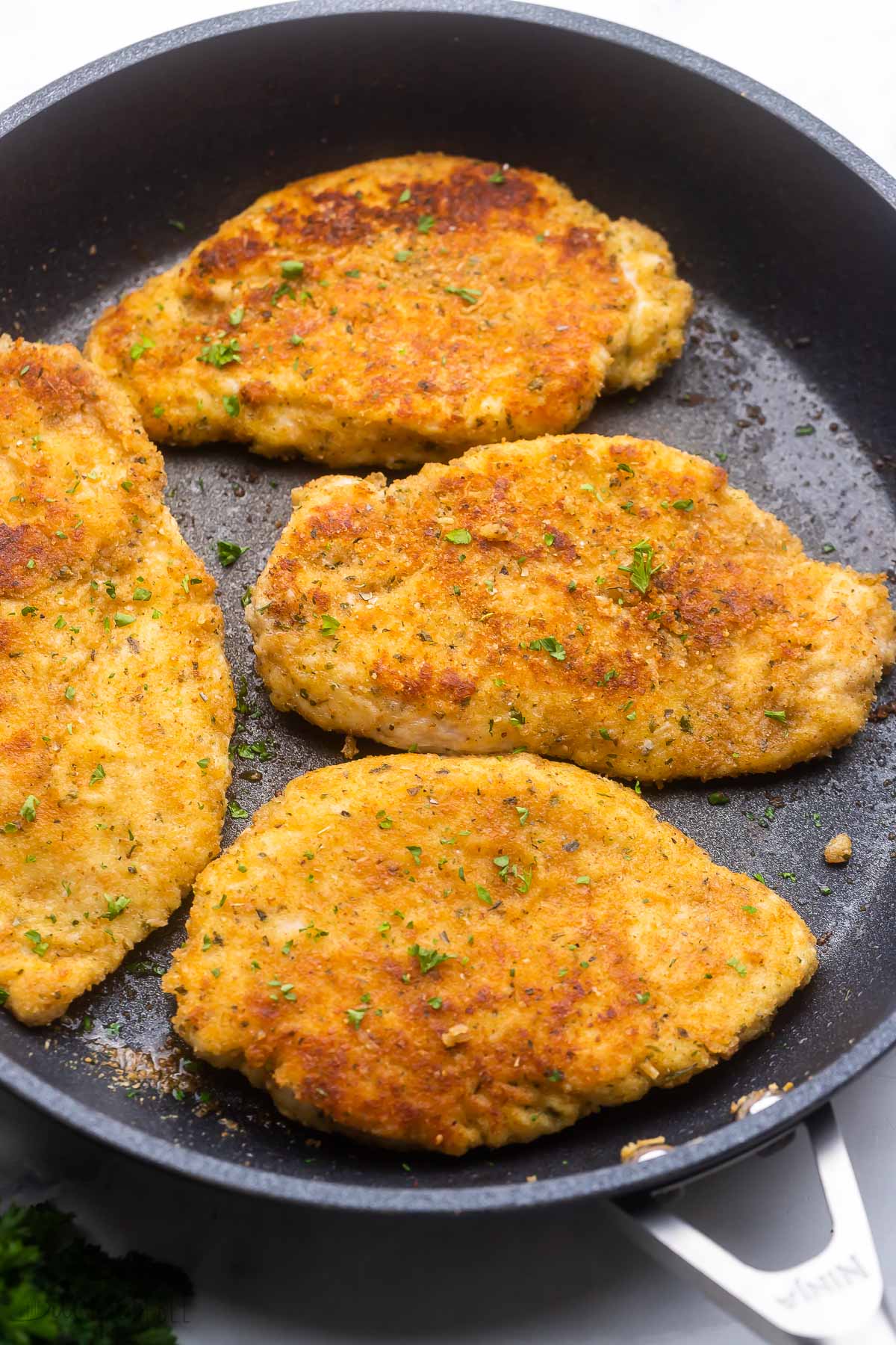 close up of parmesan crusted chicken breasts in black frying pan.