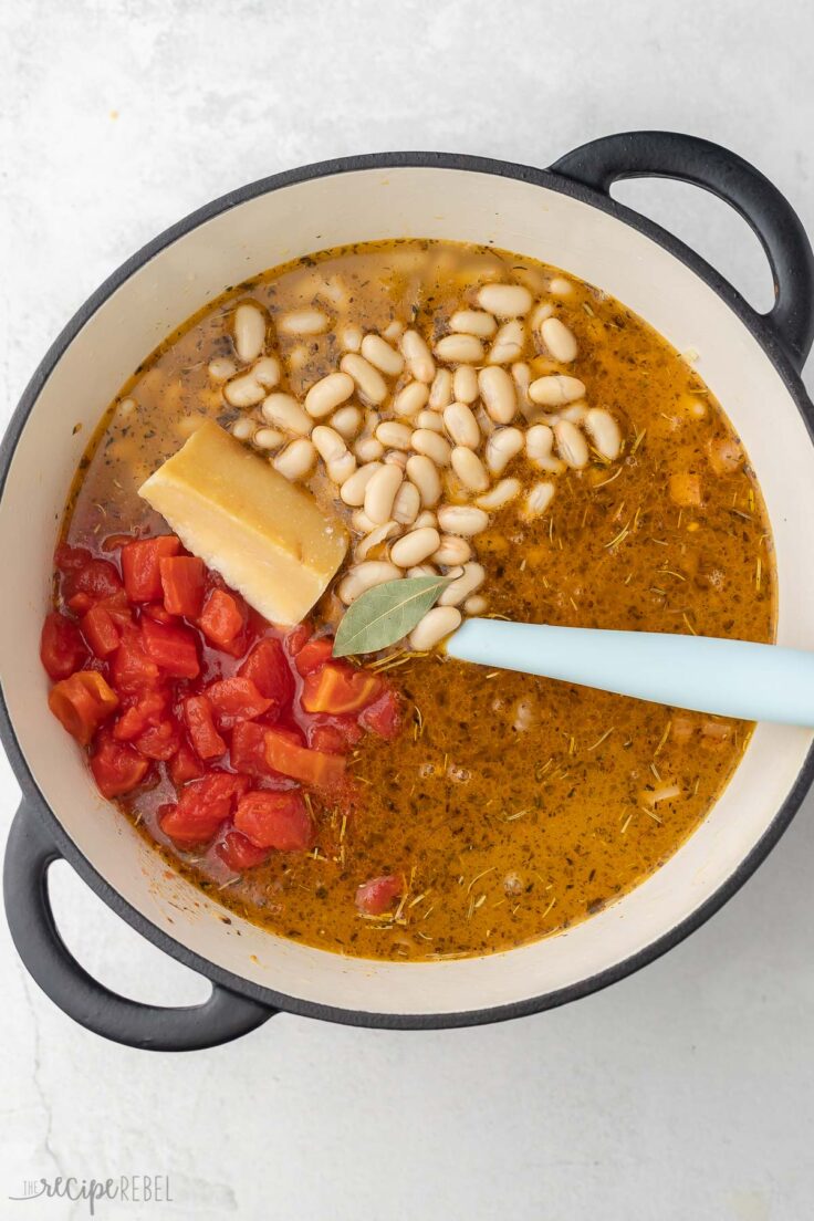 large pot full of pasta fagioli ingredients with parmesan rind and bay leaf added to top.