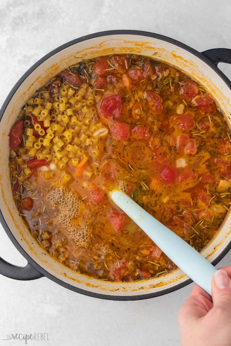 large pot of cooked pasta fagioli being stirred with blue spatula.