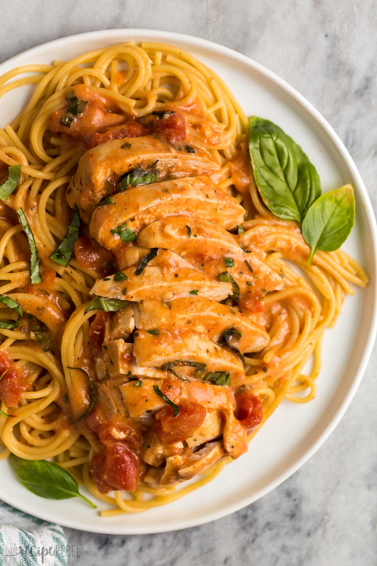 close up image of sliced slow cooker tomato basil chicken breasts over pasta.