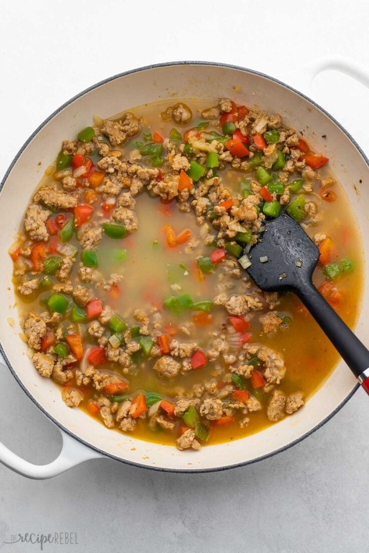 spatula in white pan and broth added to ingredients.