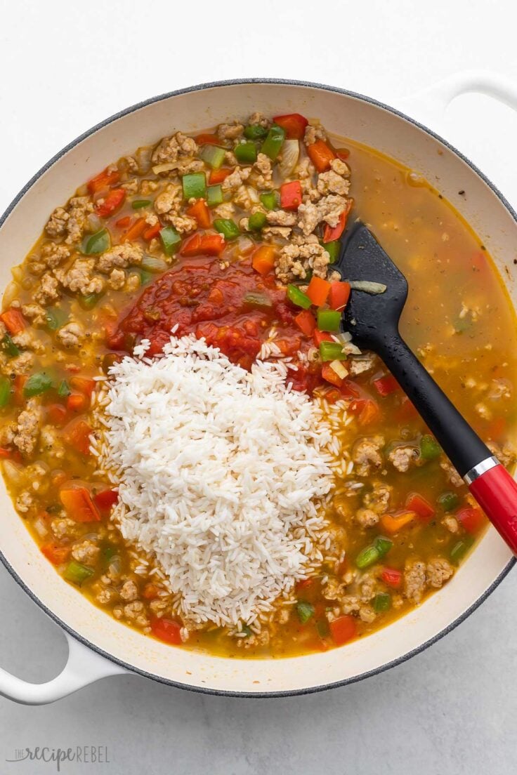 rice and salsa added to white pan of stuffed pepper casserole.